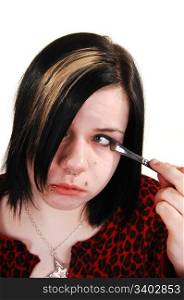 A close up of a young girl with dark hair doing her eye makeup with a smallbrush, for white background.