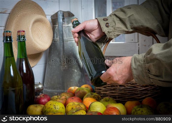 a close up of man hands with a bottle of cider and apples