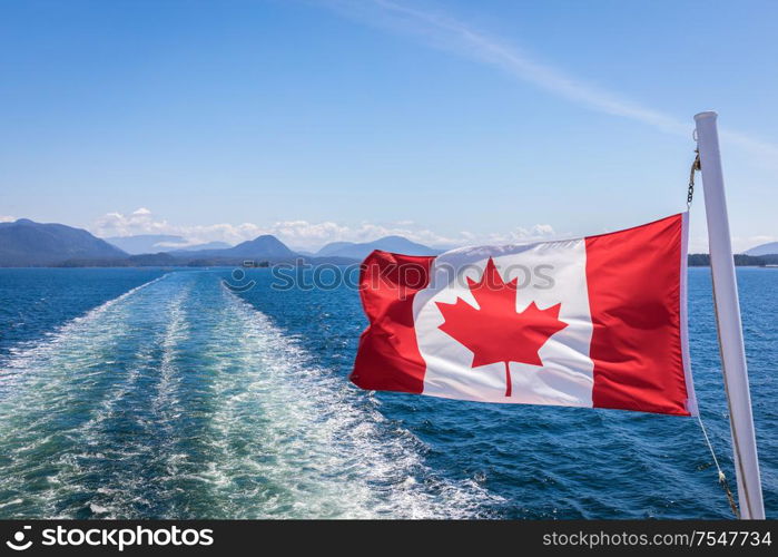 A close up of the Canadian flag flying in the wind at the back of ferry as the boat makes it way through the Inside Passage, British Columbia, Canada