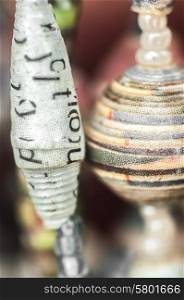 A close up view of necklaces made partly from paper beads hanging from a display. Viewed up close the letters on the paper are still visible on the white beads.