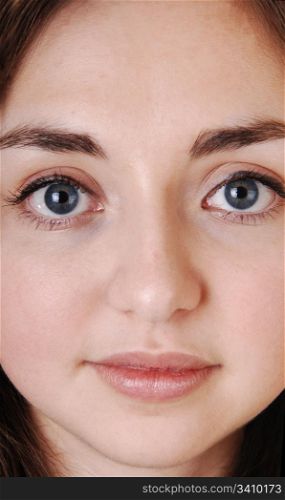 A closeup of a beautiful face of a young girl with blue eyes and brunettehair, looking strait into the camera.