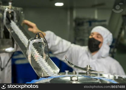 A closeup of the production of medical syringes with worker in a mask on blur background. Closeup of the production of medical syringes with worker in a mask on blur background