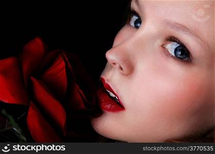 A closeup picture of a lovely girls face with a red rose and blue eye&rsquo;s, isolated on black background.