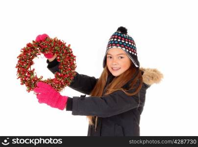 A closeup picture of a young pretty girl holding up a colorful adventswreath, in a jacket, mittens and hat, isolated on white background.