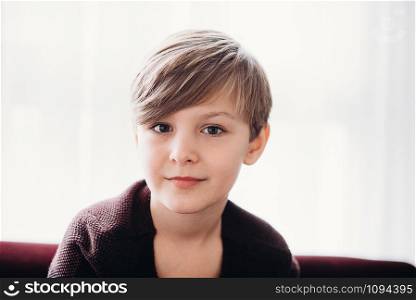 a closeup portrait of a cute boy kid sitting on a sofa against the light window, soft focus