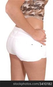 A closeup shot of the bum of a young girl in a beige blouse and whiteshorts with her hand on her hip, for white background.