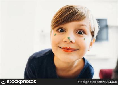 a closeup view of a cute boy with a face painted with eatable bright color cream, smiling with clown lips