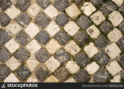 A cobblestone sidewalk in the Alfama neighhborhood of Lisbon has arranged the light and dark stones in an alternating pattern like a checkboard.