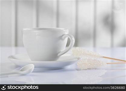 a coffee cup with spoon and sugar stick on white table