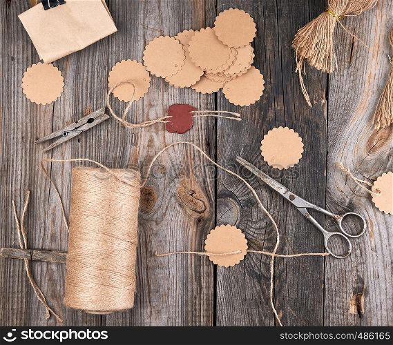 a coil of brown rope, paper tags and old scissors on a gray wooden background, objects for making handicrafts