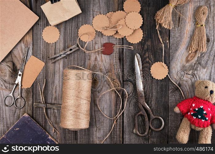 a coil of brown rope, paper tags and old scissors on a gray wooden background, objects for making handicrafts
