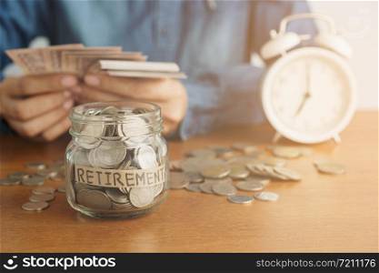 A coin in a glass bottle Image blurred background of business people sitting counting money and a retro white alarm clock, Investment business, retirement, finance and saving money for future concept.