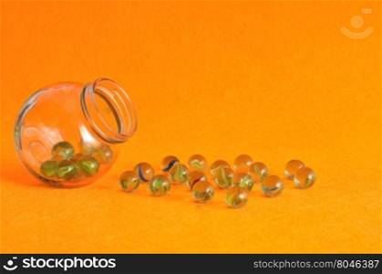 A collection of marbles in a glass jar displayed on an orange background