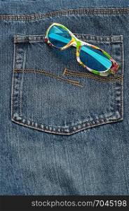 A colorful pair of sunglasses in the back pocket of a denim jeans pants.