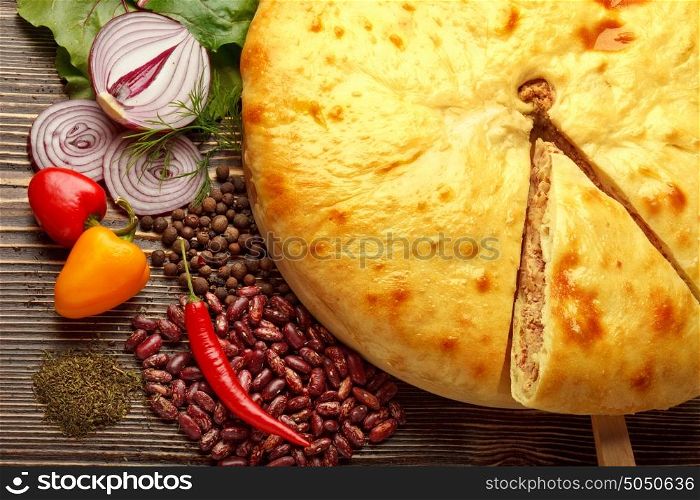 A colorful photo of traditional delicious beef osetinian pie. Kadurdjin meat pie and vegetables on wood.