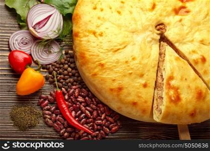 A colorful photo of traditional delicious beef osetinian pie. Kadurdjin meat pie and vegetables on wood.