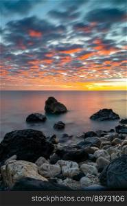 A colorful sunrise at Cala Gonone with black and white rocks and boulders in the foreground