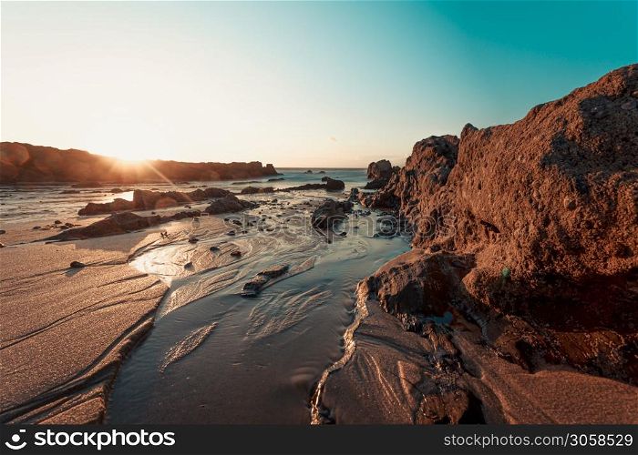 A colorful sunset on the beach over the rocks filled with mussels