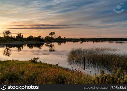 A colorful sunset over a calm lake with reflections and reeds in the foreground