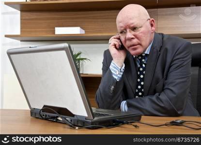 A company director talking on his mobile telephone whilst in front of his laptop