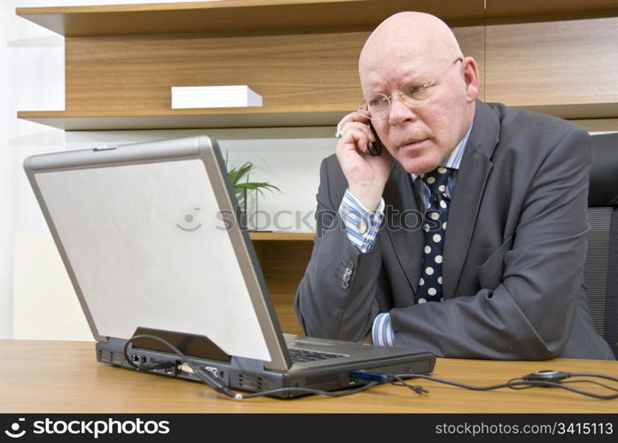 A company director talking on his mobile telephone whilst sitting in front of his laptop