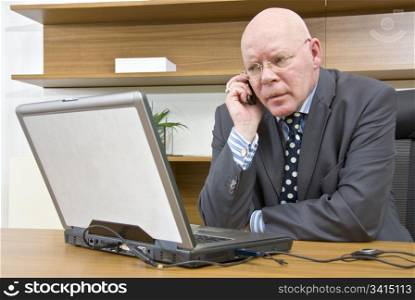 A company director talking on his mobile telephone whilst sitting in front of his laptop