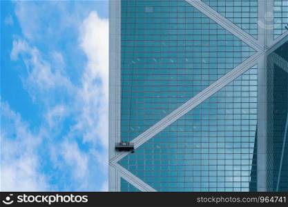 A company group of people, workers or washers, cleaning windows glass on a high rise office building with cable wires outside in Hong Kong Downtown, urban city at noon with blue sky.