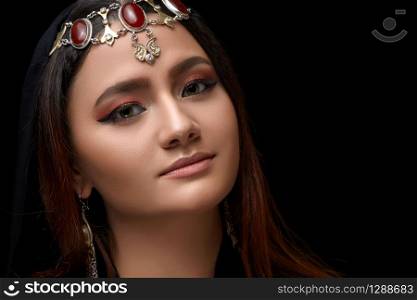 A conceptual middle Eastern portrait of a woman&rsquo;s face decorated with Oriental-style jewelry on a black Studio background.