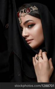 A conceptual middle Eastern portrait of a woman&rsquo;s face decorated with Oriental-style jewelry on a black Studio background.