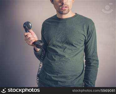 A concerned and worried looking young man is holding the receiver of a vintage rotary phone