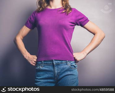 A confident young woman in purple shirt is standing in a powerful pose with her hands on her hips