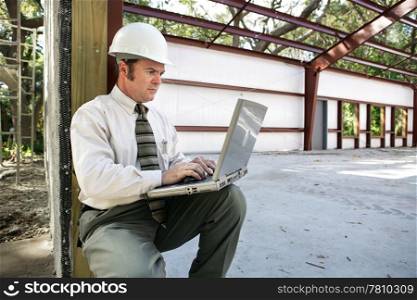 A construction engineer or inspector on the construction site with his laptop.