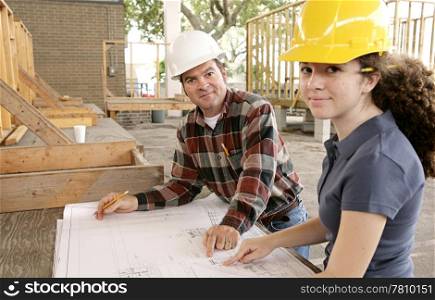 A construction foreman going over the blueprints with a female apprentice.