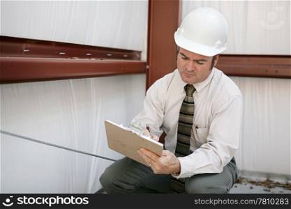A construction inspector on a jobsite making notations on his clipboard.