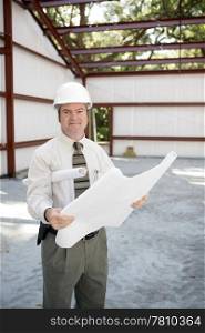 A construction inspector on the job site holding blueprints and smiling.