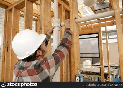 A construction worker connecting plumbing pipe in an unfinished wall. Focus is on the connecting pipes.