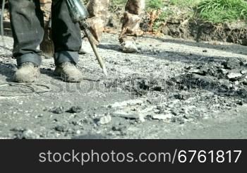 A construction worker operates a jackhammer to break up asphalt on a road