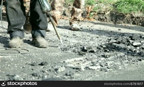 A construction worker operates a jackhammer to break up asphalt on a road