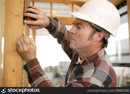 A construction working taking measurments and marking a wood beam on a house frame.