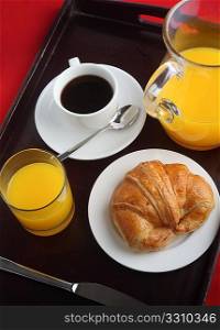 A Continental breakfast on a tray over a red cloth, comprising orange juice, black coffee and a croissant