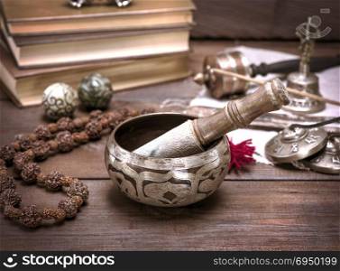a copper singing bowl and a wooden stick on a brown table, next to a rosary