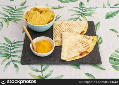 a corn or wheat tortilla, folded in half that can be filled with cheese, beans and chicken and eaten hot, either fried or cooked on the comal with corn chips and melted cheddar cheese