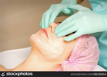 A cosmetologist is applying cream on the fema≤face, close-up view. Woman with doctor beautician in beauty clinic. A cosmetologist is applying cream on the fema≤face, close-up view. Woman with doctor beautician in beauty clinic.