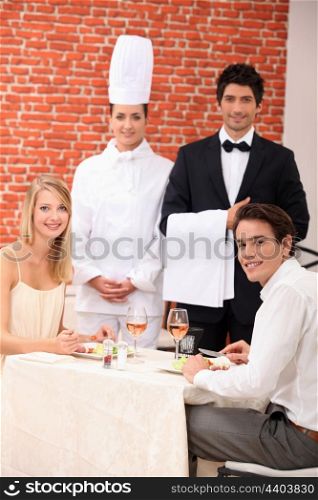 A couple being served by a waiter and a chef in a restaurant
