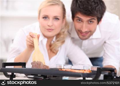 a couple facing the camera and showing meat cooked on an electric plancha cooker