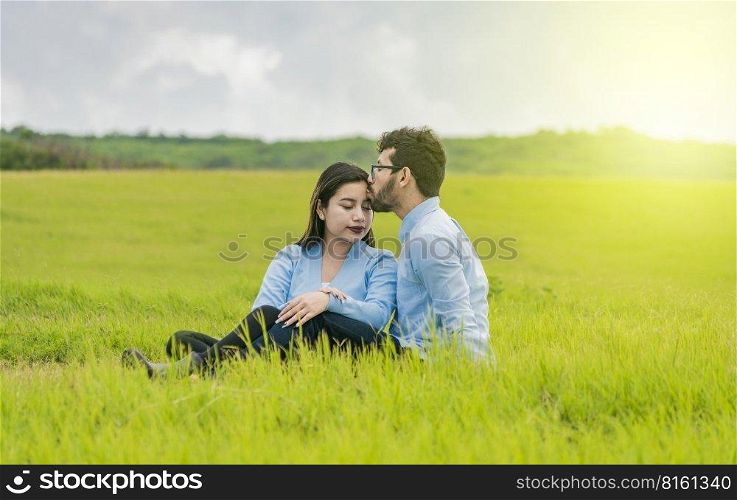 A couple in love sitting in the field kissing their foreheads, A man kissing his girlfriend’s forehead in the field, Romantic couple sitting in the grass kissing their foreheads