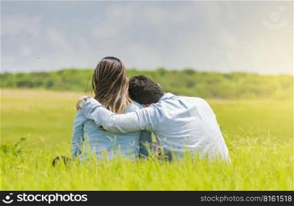 A couple in love sitting on the grass hugging from the back, a romantic couple sitting on the grass hugging from the back, rear view of a couple in love hugging on the grass