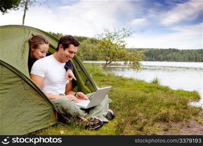 A couple looking at a computer while camping in a tent