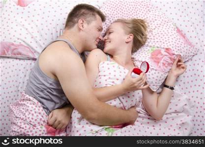 A couple lying in bed. Man gives a woman a ring. The girl did not expect such a ?????? and happy. Photo on top