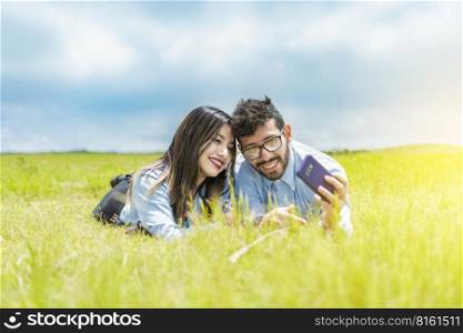 A couple lying on the grass taking a selfie, young couple in love lying on the grass taking a selfie, two people in love lying on the grass taking selfies